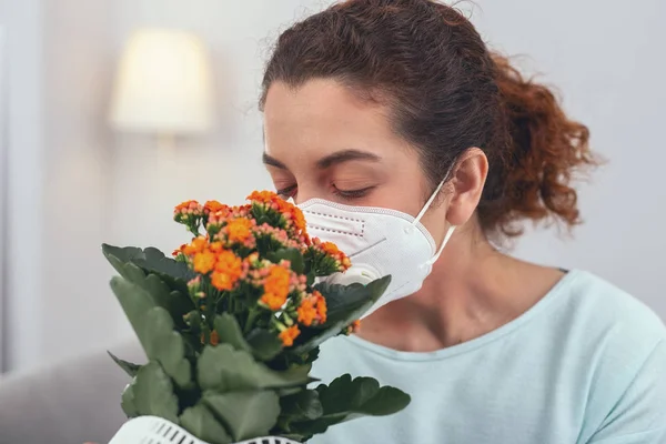 Chica joven oliendo una flor en maceta mientras usa una máscara respiratoria — Foto de Stock