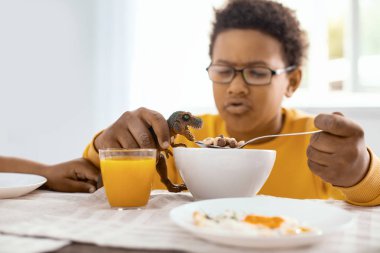 Oyuncak dinozor ile kahvaltıda oynayan sevimli pre-Teen Çocuk