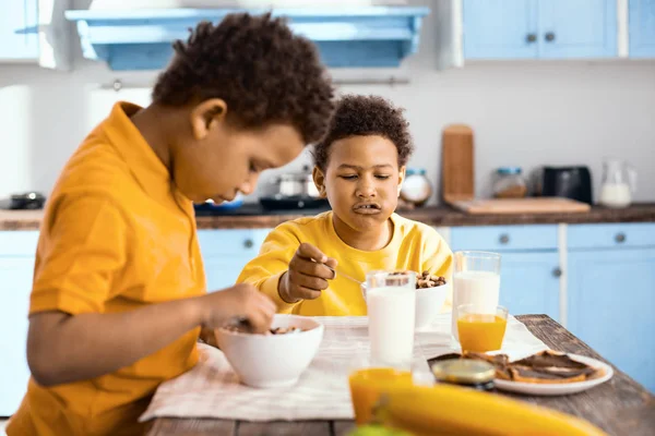 Niños preadolescentes de pelo rizado comiendo cereales y hablando —  Fotos de Stock