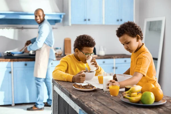 Pleasant children eating breakfast while their father cooking — Stock Photo, Image