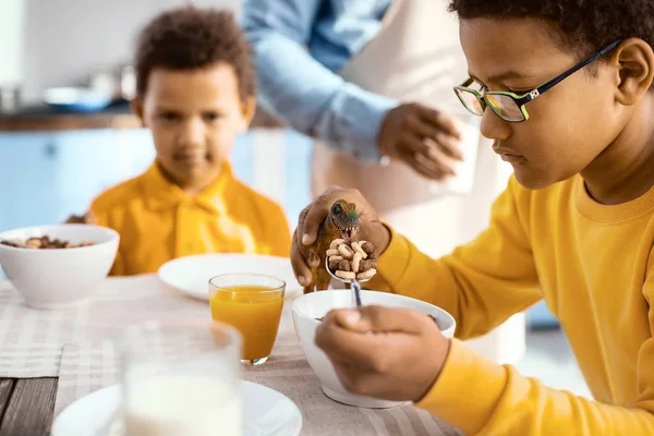 Cute pre-teen boy feeding his toy dinosaur with cereals — Stock Photo, Image