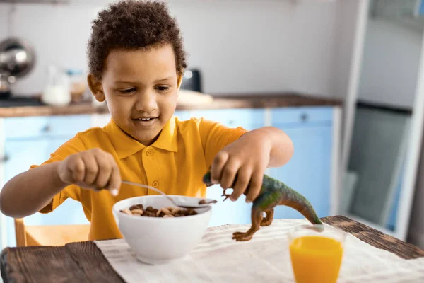 Cheerful little boy giving food to his toy dinosaur