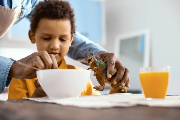 Pečující rodič pomáhat jeho malý syn krmiva hračka dinosaurus — Stock fotografie