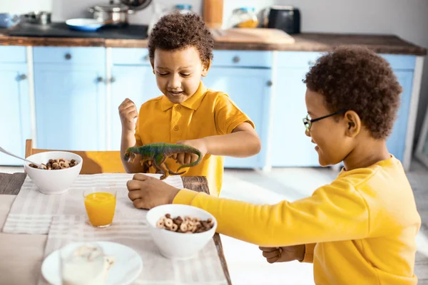 Pleasant little kids playing with dinosaur while having breakfast — Stock Photo, Image