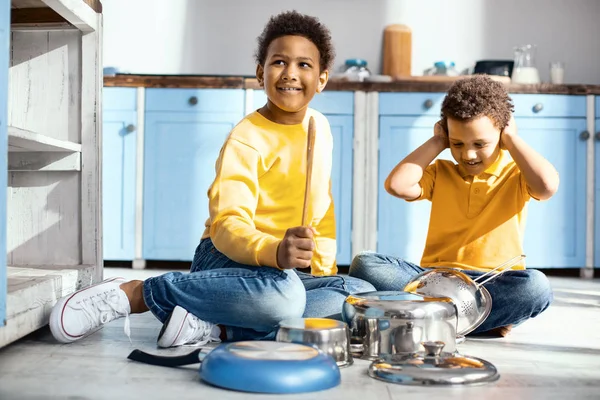 Aufmunternde kleine Jungen, die laute Geräusche erzeugen, indem sie auf Töpfen trommeln — Stockfoto