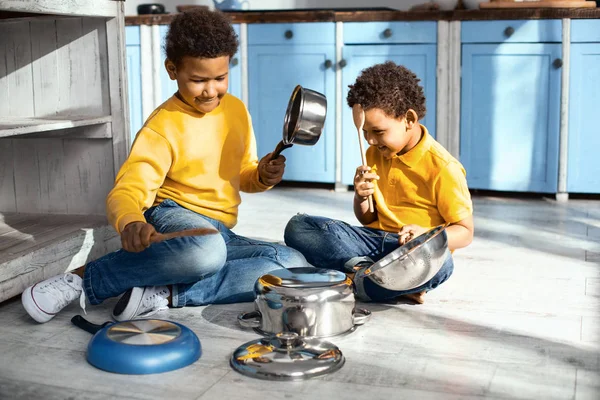 Verschmitzte kleine Jungen erzeugen Kakophonie, indem sie auf Kochtöpfen trommeln — Stockfoto