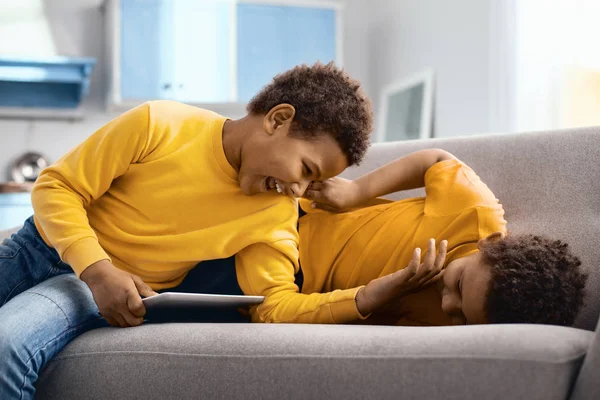 Joyful little brothers tickling one another on sofa — Stock Photo, Image