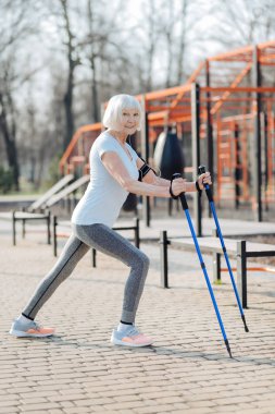 Gülümseyen kadın egzersiz yaparken koltuk değneği kullanarak