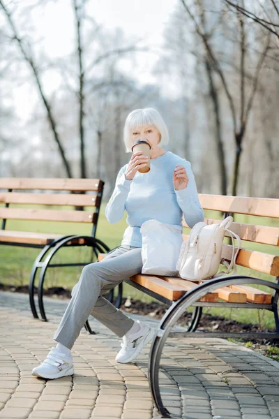 Предупредите женщину, пьющую кофе, сидя на скамейке — стоковое фото