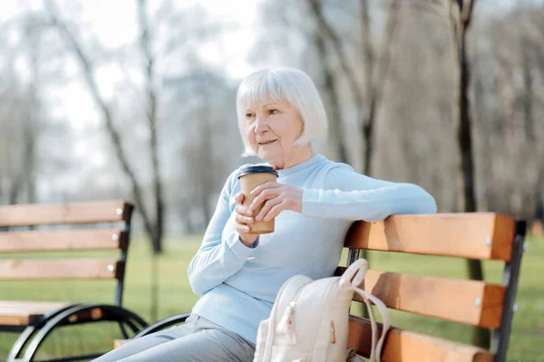 Mulher atenciosa bebendo café enquanto sentada no banco — Fotografia de Stock