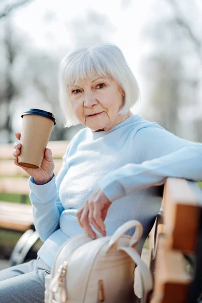 Mujer concentrada bebiendo café mientras está sentada en el banco — Foto de Stock