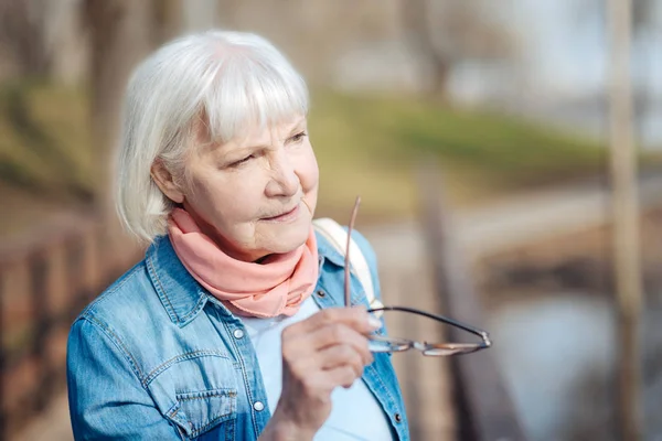 Serious old woman holding her glasses — Stock Photo, Image