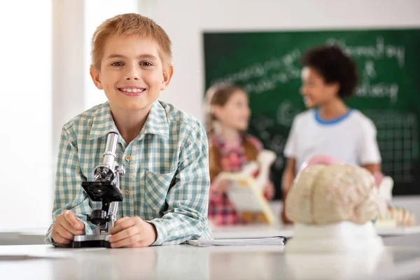 Веселий щасливий школяр стоїть перед мікроскопом — стокове фото