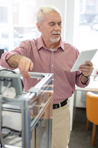 Чарівний старший чоловік читає інструкцію з 3D принтера з планшета — стокове фото