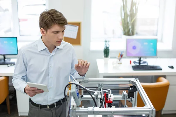 Очаровательный молодой человек наблюдает за механизмом 3D-принтера — стоковое фото
