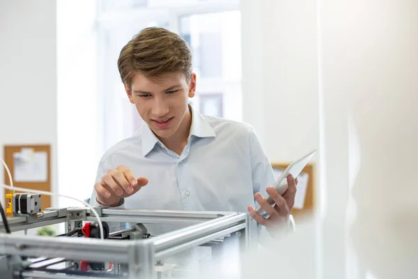 Young office worker smiling and peeking inside 3D printer — Stock Photo, Image