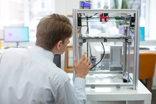 Agradable joven ingeniero viendo impresora 3D en acción — Foto de Stock