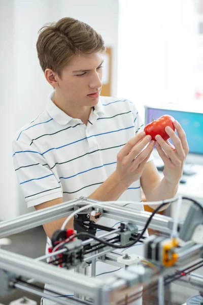 Jovem engenheiro agradável escrutinando tomate vermelho impresso — Fotografia de Stock