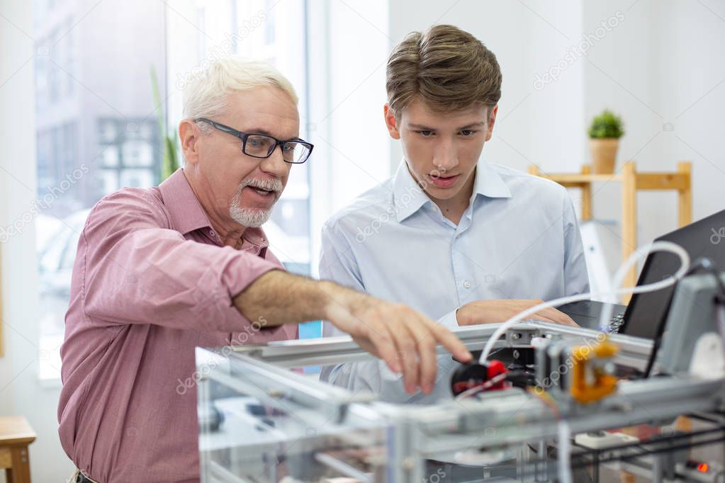 Experienced senior engineer instructing intern about 3D printers