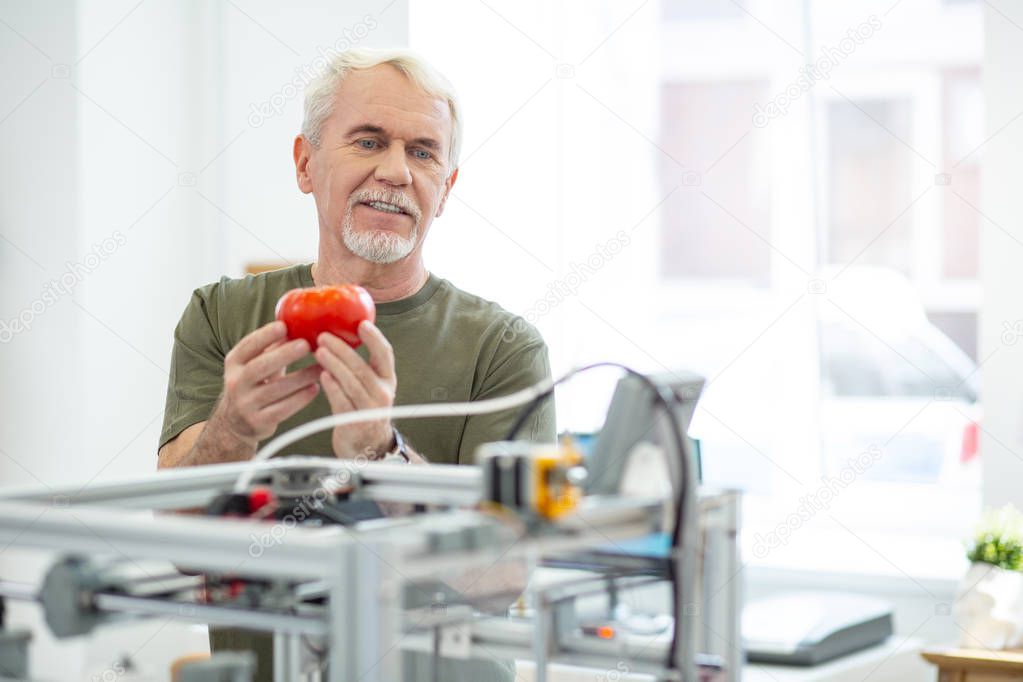 Joyful senior man admiring red tomato printed with 3D printer