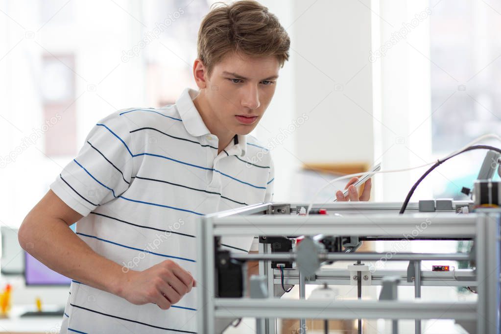 Pleasant young man monitoring performance of 3D printer