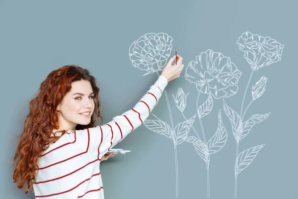 Mujer alegre sonriendo mientras dibuja una flor — Foto de Stock