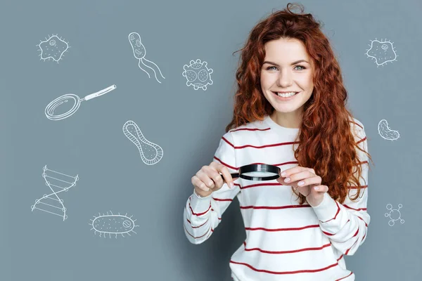 Happy young woman holding a magnifying glass and looking at cells — Stock Photo, Image