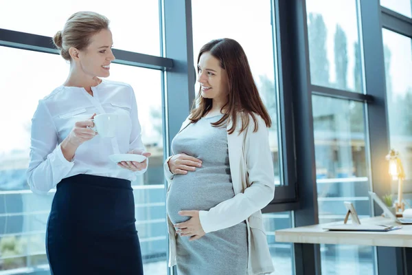 Довольная беременность, стоящая рядом с коллегой — стоковое фото