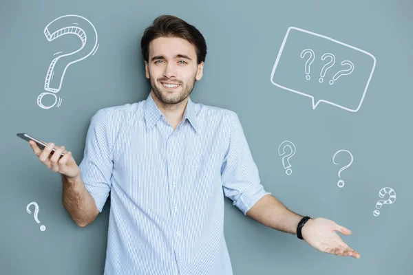 Positive man shrugging his shoulders while standing with a smartphone — Stock Photo, Image