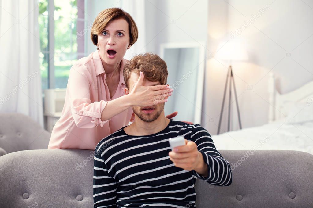 Shocked aged woman covering her sons eyes