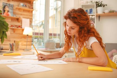 Ahşap çalışma masada oturan kızıl saçlı moda tasarımcısı