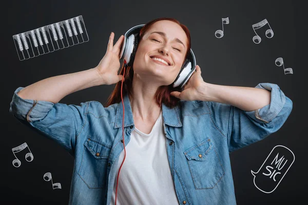 Ung kvinna ler och stänga hennes ögon medan du lyssnar på musik — Stockfoto