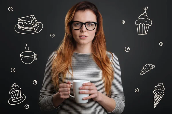 Schöne Frau trinkt Tee und denkt darüber nach, Süßigkeiten zu essen — Stockfoto