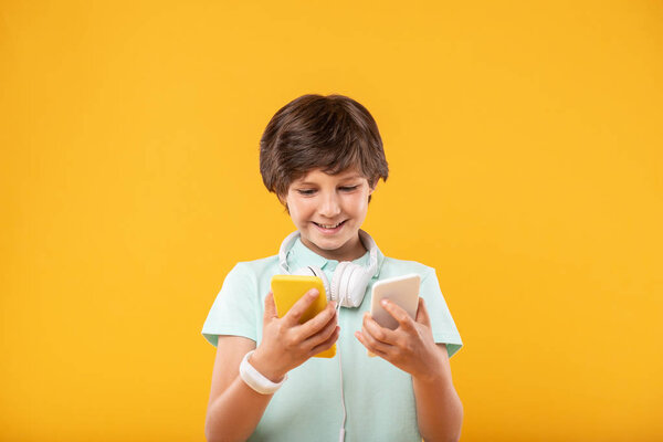 Joyful schoolboy having two phones