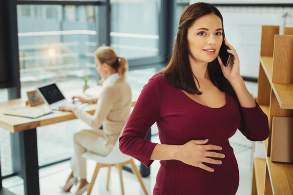 Beautiful pregnant woman touching her belly while talking on the phone — Stock Photo, Image