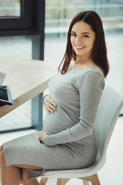 快適な期待 彼女のモダンなオフィスのテーブルに座って彼女の腹に触れて美しい若い妊婦秘書 — ストック写真