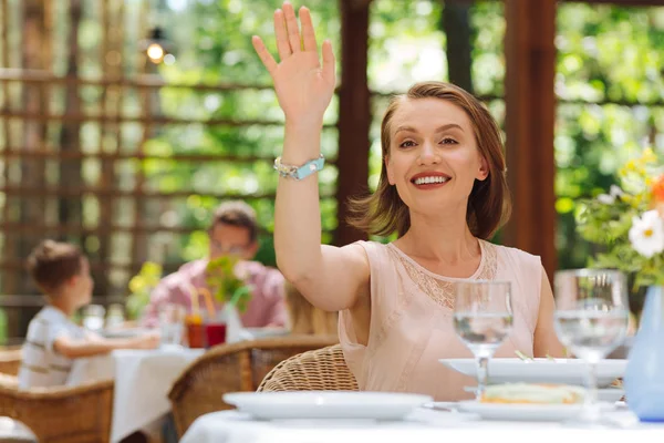 Sonriente mujer de ojos oscuros levantando la mano llamando a la camarera —  Fotos de Stock