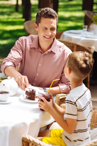 Father in pink shirt eating dessert with his little son