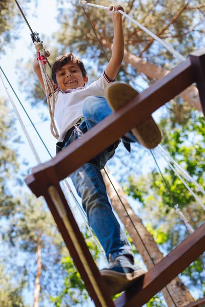 Alegre niño preadolescente dando un paso mientras trepa en el parque de cuerdas —  Fotos de Stock