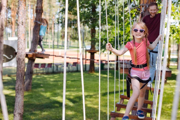 Pequeña niña caminando a lo largo del puente de cuerda en el parque de aventuras — Foto de Stock