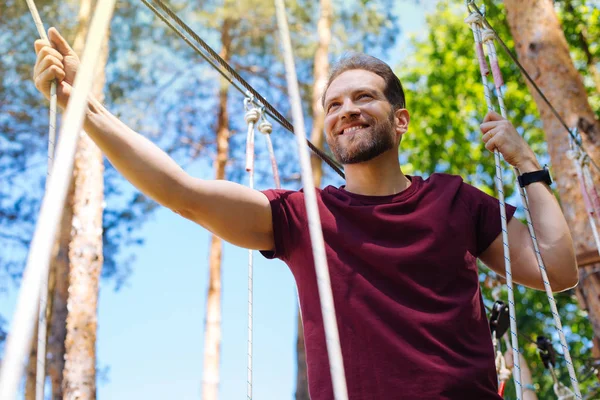 Веселый молодой человек, лазающий по веревочному парку — стоковое фото