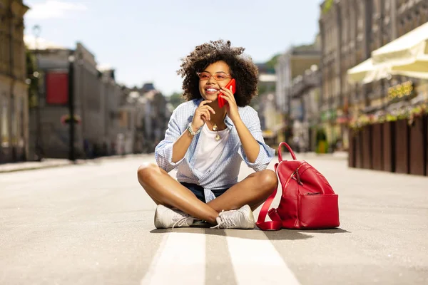 Asfalt üzerinde otururken telefon görüşmesi neşeli kıvırcık kadın