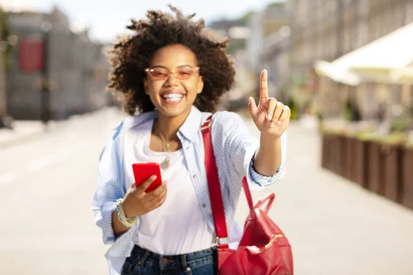 Mujer encantadora levantando el dedo y usando el teléfono — Foto de Stock