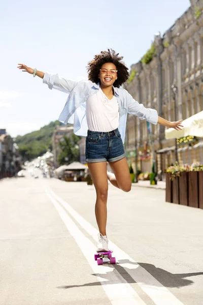 Upbeat curly flicka poserar med ena benet skateboard — Stockfoto