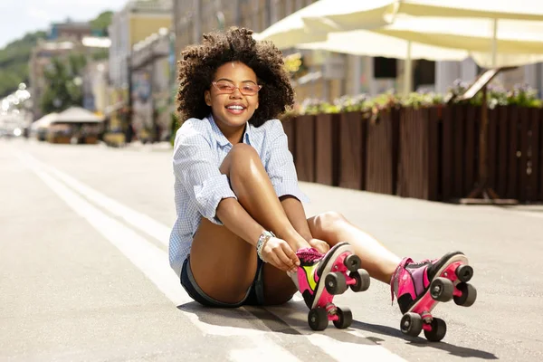 Chica rizada alegre sonriendo mientras se pone patines —  Fotos de Stock