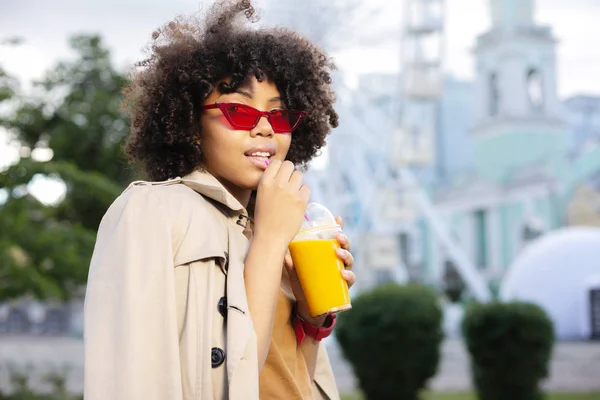 Pretty curly woman sipping orange juice in the street — Stock Photo, Image