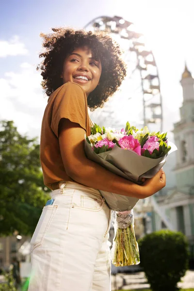 Agradable mujer rizada posando con flores durante el cumpleaños —  Fotos de Stock