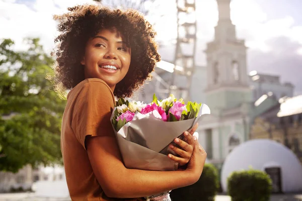 Mujer bastante rizada sosteniendo flores y sonriendo —  Fotos de Stock