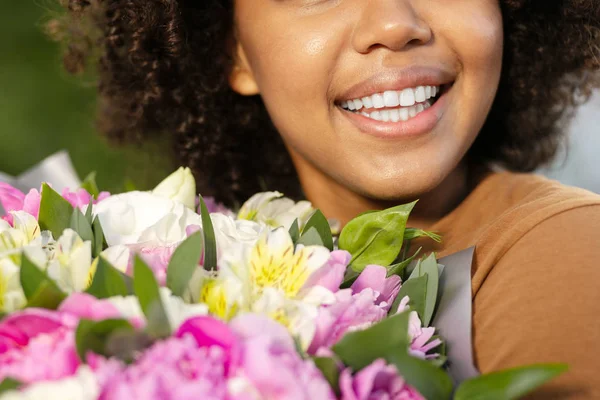Close up of a curly woman smiling and holding flowers — Stock Photo, Image