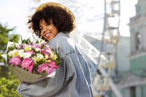 Jovencita alegre en sombrero de paja sosteniendo flores —  Fotos de Stock